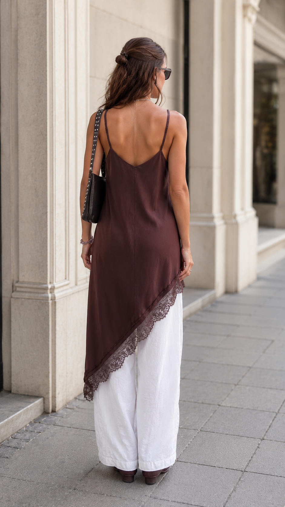 Back view of chocolate brown asymmetric lace trim slip tunic layered over white wide-leg pants