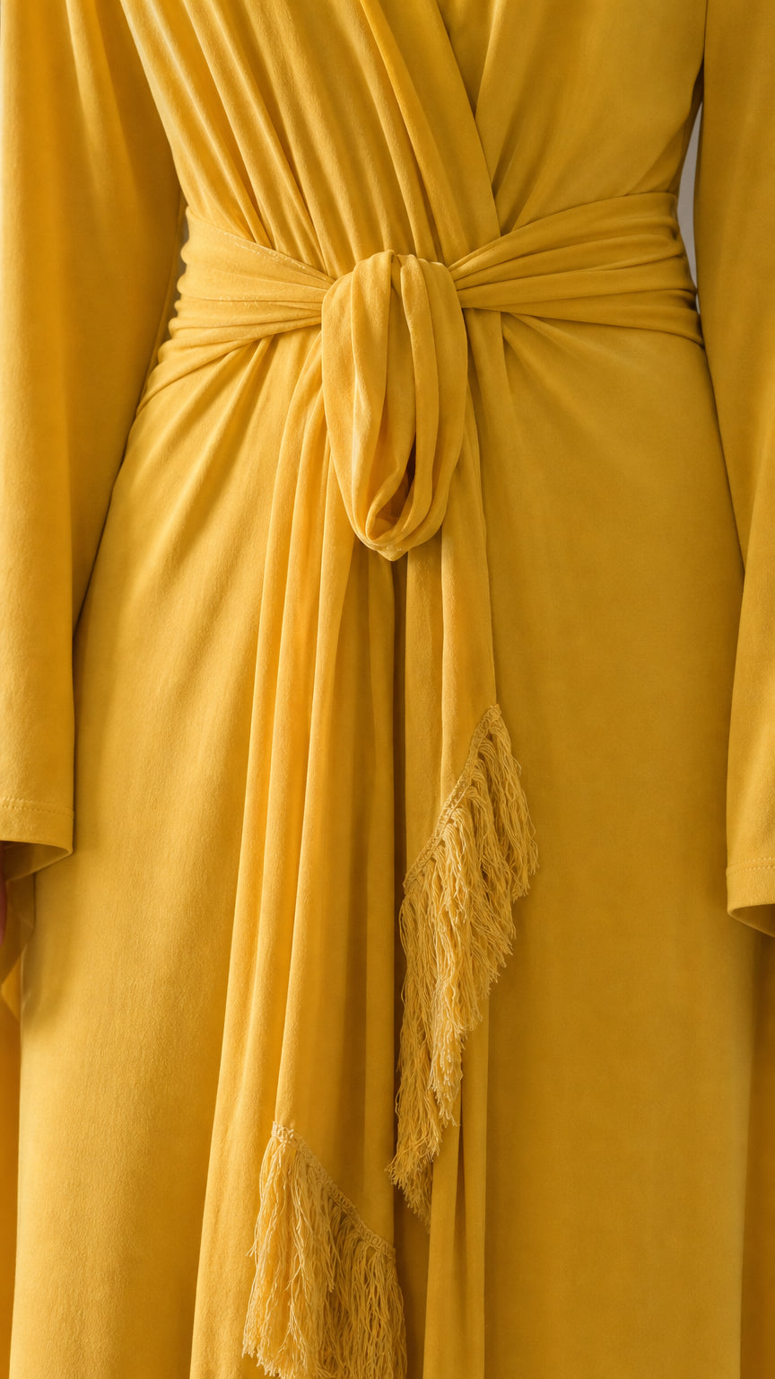 Close-up detail of the waist tie and fringe trim on yellow dress