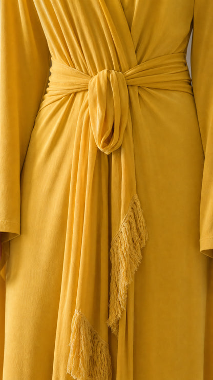 Close-up detail of the waist tie and fringe trim on yellow dress