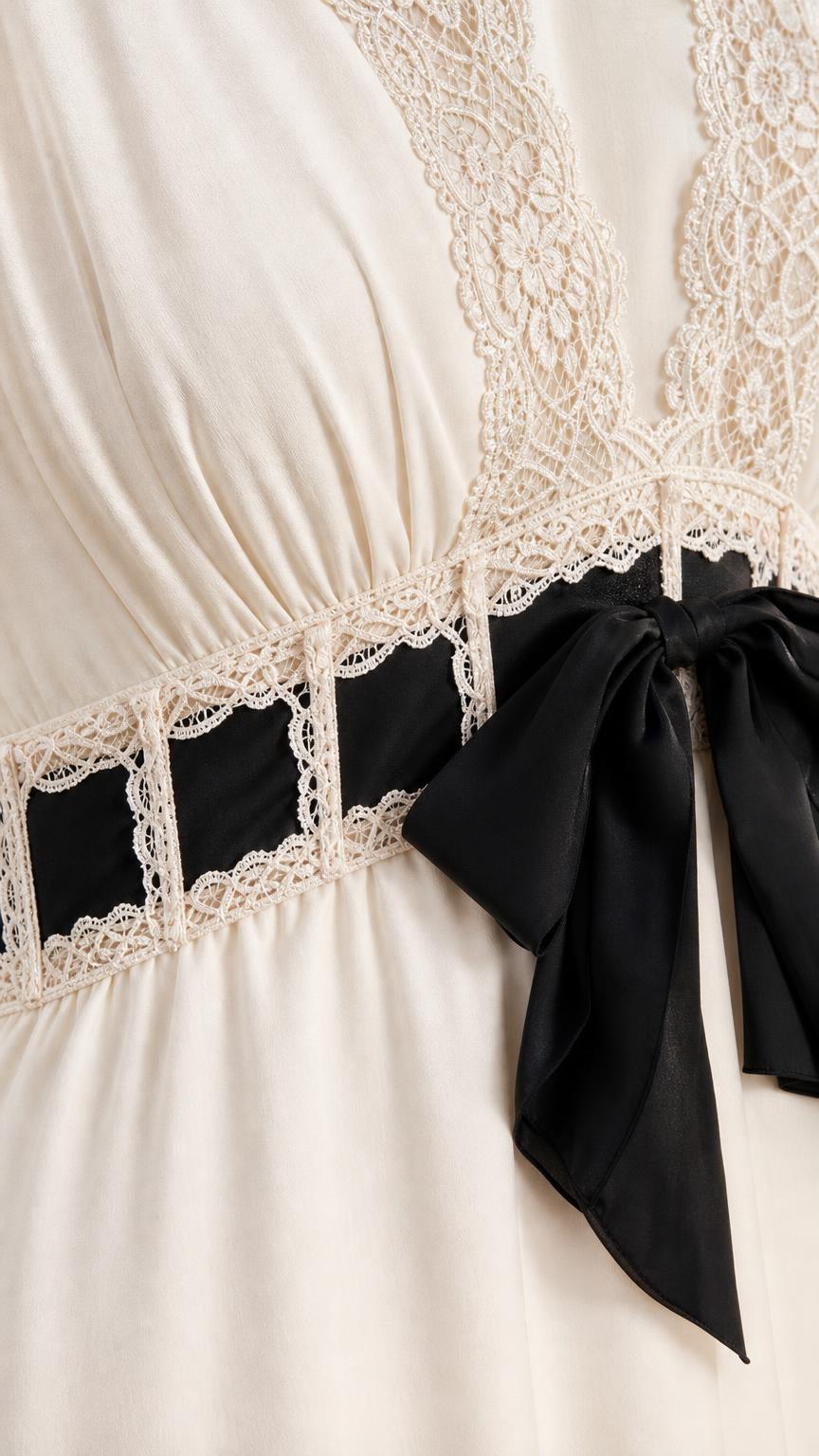 Close-up detail of lace neckline and black bow waist accent on ivory dress