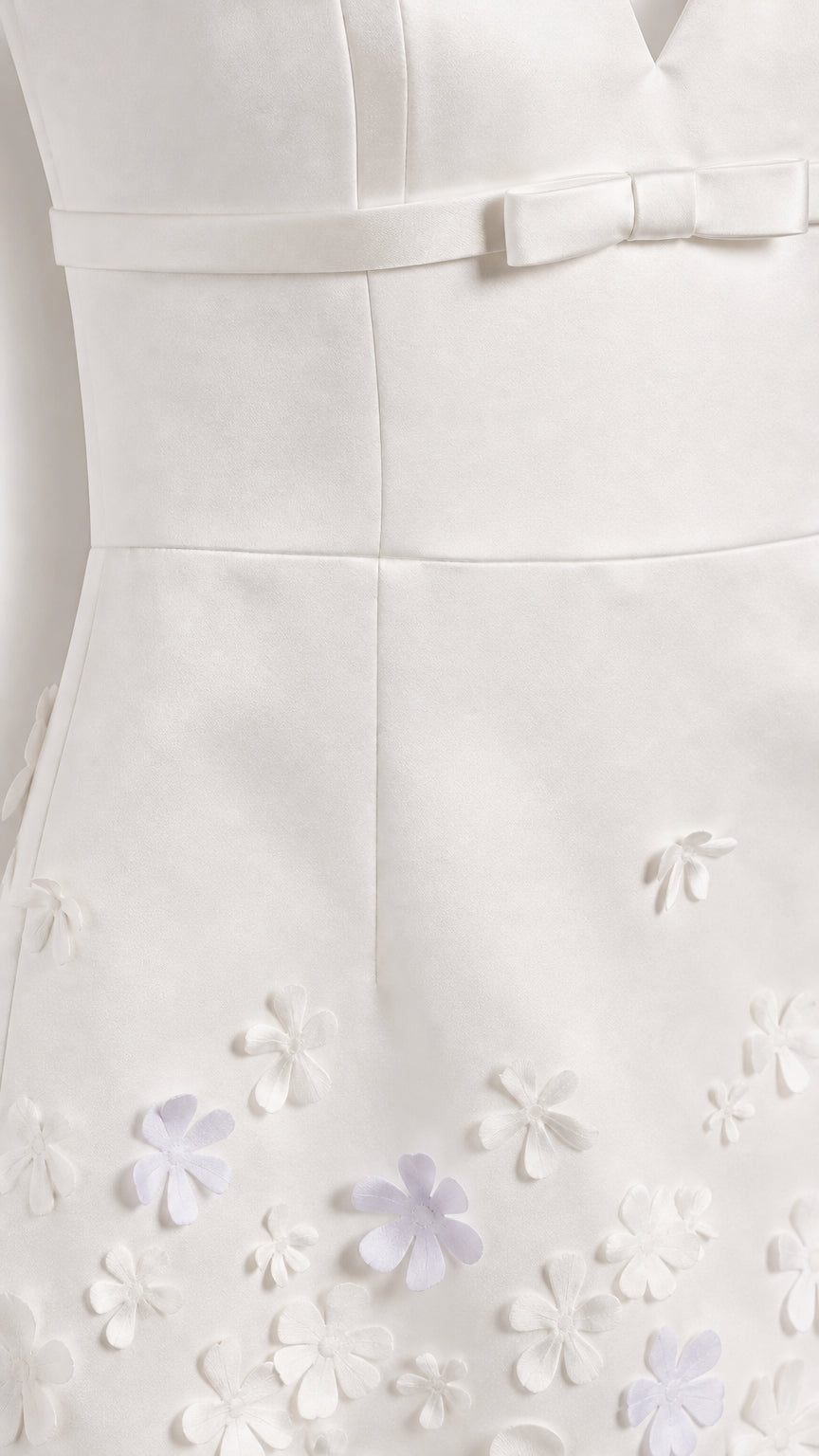 Close-up of white mini dress bodice bow and 3D floral hem