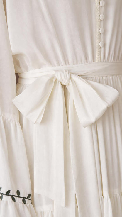 Close-up of the ivory dress tie waist, gathered fabric, buttons, and decorative sleeve trim